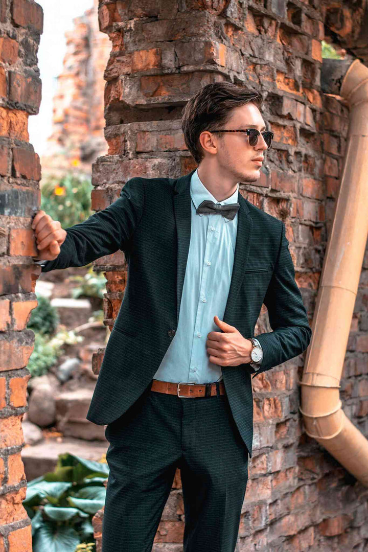 a man in a suit and bow tie leaning against a brick wall