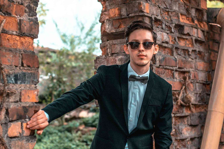 a man in a suit and bow tie leaning against a brick wall